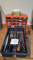 Orange plastic small parts organizer with transparent drawer compartments and tray containing various hand tools on the workbench.