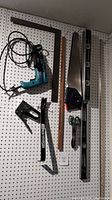 Tools hanging on a pegboard showing a Makita hammer drill, staple tool, two hand saws, a 48-inch Mastercraft level, a ruler, a framing square, and a paint can opener.