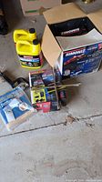 Image showing two yellow 4L jugs of Motomaster antifreeze, Simoniz car cleaning kit box, tire iron, and air inflation product box on a concrete floor.