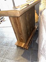 Side view of retro bar showing padded leather-like front with button tufting and wood grain finish.