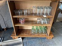 Shelving unit with multiple sets of clear glassware including highball, streetcar, green-tinged Coke glasses, and other drinking glasses