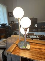 Three-light bar lamp with white globe shades lit, on a wooden side table in living room.