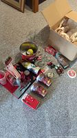 Photo showing assortment of Coca Cola memorabilia items including tins, cans, glass cups, miniature ornaments, and straws on a carpeted floor.