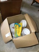 Open cardboard box showing plates, bowls, mugs, and Sony waist pouch inside