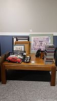 Full view of the coffee table with various unrelated items on top including framed art, model cars, and CDs as reference for table size and use.