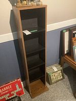 Wooden shelf unit with black shelves shown from front, illustrating the shelf spacing and size relative to the nearby Scrabble game box and framed art.