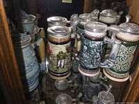 Front view of four collectible steins grouped closely showing various designs and pewter lids.