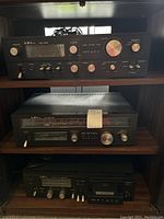 Front view of three stacked LXI Series stereo components on wooden shelves, including the AM4002 amplifier on top, TR6002 tuner in middle, and DK5002 cassette deck on bottom.