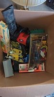 Photo of a large box filled with assorted tools including a power tool, hammer, and packaged items.