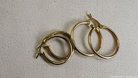 Two pairs of gold vermeil hoop earrings laid on white fabric, showing smooth polished finish.