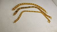 Three handmade gold-tone bracelets displayed flat showing their woven and chain designs with S-clasps visible.
