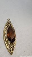 Front view of elongated gold-tone antique pendant with brown faceted oval stone and detailed floral design.