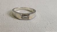 Close-up of the front view of the silver tone ring with a rectangular clear gemstone channel set in the band.