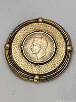 Front view of large brooch centered by George VI medallion with textured metal surrounding and decorative ball details at four equidistant points.