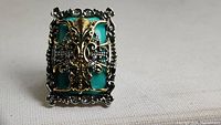 Front view of the large rectangular ring with green stone and intricate silver and gold-tone filigree work
