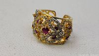 Front view of large handmade gold ring set with numerous rubies and diamonds showing ornate pattern.