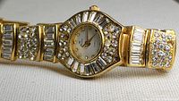 Front view of vintage Runica women's watch showing rhinestone encrusted gold-tone watch face and band with quartz movement indication on dial.