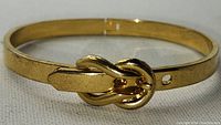 Front view of the gold tone metal bangle bracelet showing the detailed buckle clasp as closure.