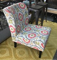 Photo of side angle showing fabric pattern and black legs of an armless upholstered accent chair on a carpeted floor.