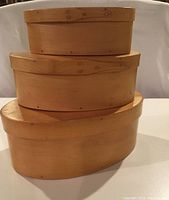 Front view of three nested oval bamboo boxes with lids, showing smooth light wood and top closed lids.