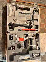 Plastic carry case open displaying assortment of metal and plastic bike repair tools including wrenches, chain whip, crank remover, screwdrivers, and tire levers.
