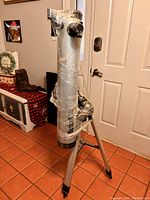 Full view of the silver telescope mounted on an aluminum tripod wrapped in protective plastic.