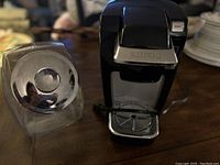 Glass cookie jar with metal lid and Keurig coffee maker on wooden surface.