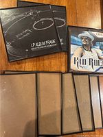 Eight black-framed LP album display frames arranged on wooden surface, showing fronts and backs, with one frame displaying Kid Rock album cover.