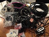Photo showing assorted cords, headphones, and electronics accessories on a surface, including auxiliary and USB cables and cleaning wipes.
