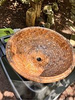 Round ceramic sink with mosaic tile pattern in rustic earth tones on black surface outside under sunlight.