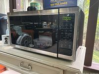 Front view of Oster microwave oven showing black and stainless steel finish with digital control panel on the right side.