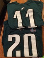 Two folded green Philadelphia Eagles T-shirts, one with number 11 and another with number 20 and Hall of Fame patch