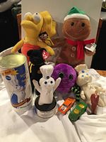 Full view showing assorted plush toys and toy cars including Lisa Simpson doll with tags, Gingerbread Man, Halloween TY Spider, Pillsbury Doughboys, and small toy cars.