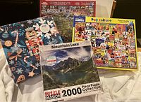 Lot of four puzzles shown stacked, includes Nutcracker puzzle, Mountain Lake puzzle, Pop Culture puzzle, Presidents puzzle.