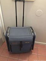 Front view of blue Fiskars rolling scrapbook tote with retracted handle and zippered compartments visible.