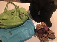 Photo showing black suede boots, animal print high heel sandals, bright lime green handbag, and bright blue handbag all grouped on a table.