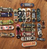 Overview of twenty Tech Deck fingerboards of various sizes and graphics laid out on wood floor.