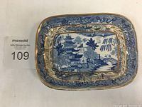Top view of a small rectangular blue and white porcelain dish with gilded edges showing detailed oriental pagoda and landscape pattern.