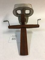 Front view of the antique stereoscope viewer, showing the eye lenses, wooden handle, and metal frame with etched design.