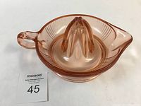 Angled front view showing the ridged reamer cone, handle, and pouring spout of the pink glass juicer.