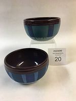 View of two small hand-thrown bowls with purple/brown rim and blue striped exterior pattern.