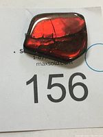 Polished ammolite gem fragment showing bright red and ruby colours with natural fissures on a white background with auction lot card.