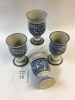 Four handmade stoneware goblets with blue slip and white leaf design, one goblet laid on its side showing base and size variation.
