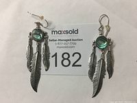 Pair of earrings showing iridescent abalone cabochons and three feather dangles per earring lying beside auction tag