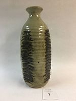 Full view of the vase showing shape and decorative glaze pattern with textured dark brown elements on light beige background.