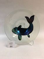 Full view of the round fused glass bowl with iridescent fish on transparent base.