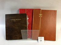 Three albums displayed: a brown 'Canada 50 Cents 1870' album, a red and an orange Uni-Safe branded albums.