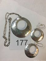 Photo of the full earring and necklace set showing two earrings with fish hook backs, a large round hammered silver pendant with an open center, and a silver Figaro chain