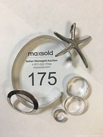 Photo showing all sterling silver jewellery pieces including bracelet, rings, brooch, star pendant, and ear cuff on a white background with auction tag 175.