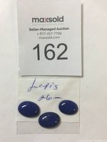 Photo of three lapis lazuli cabochons placed on a white paper with MaxSold auction number 162 showing the lot.